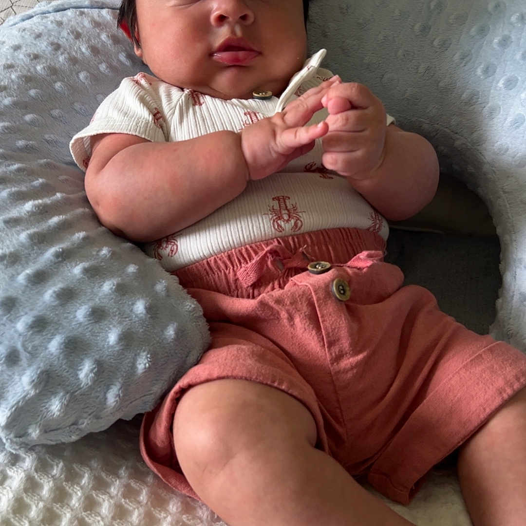 Noah is registered to the contest to win money with this photo: baby, bed, blanket, cap, child, cozy, curious, cute, face, hands, indoors, infant, pillow, pink_clothing, portrait, shorts, sitting, skin, soft_lighting, texture