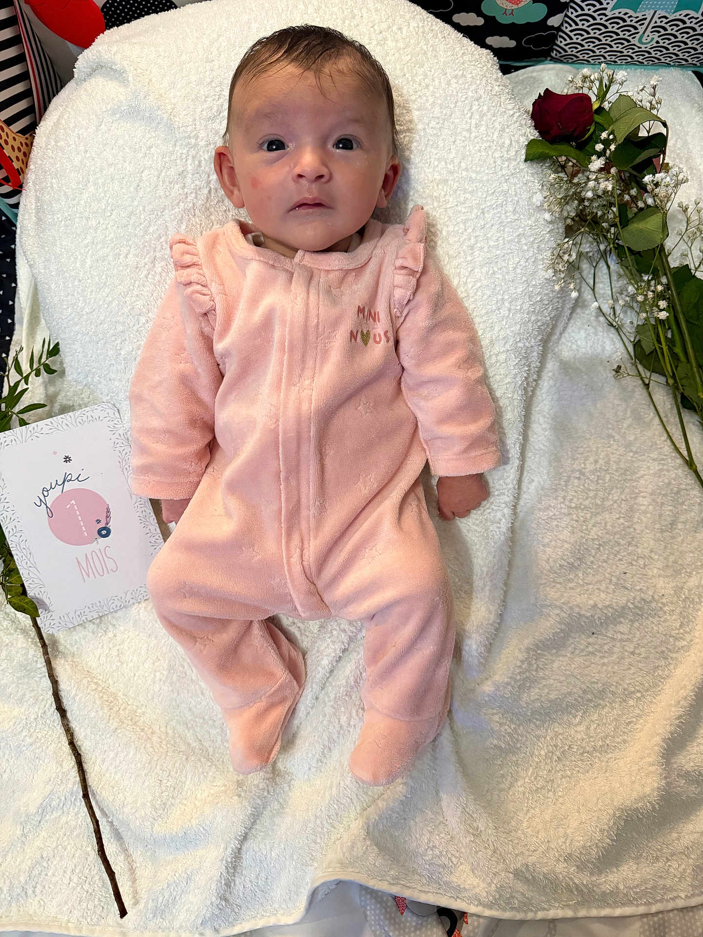 Inaya a rejoint le concours — aidez-le/la à gagner de superbes lots ! baby, infant, pink_onesie, blanket, face, portrait, flowers, card, milestone, cute, newborn, lying_down, soft_texture, indoor, white_blanket, curious_expression, child, one_month, peaceful, small
