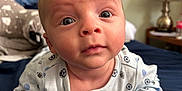 Asher is registered to the contest to win money with this photo: baby, infant, onesie, bedroom, blanket, lamp, face, eyes, expression, hand, curious, person, indoor, closeup, skin, head, young_child, sleepwear, couch, furniture