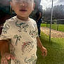 Aziel is registered to the contest to win money with this photo: toddler, child, dinosaur_shirt, grass, outdoor, daylight, stick, person, playground, fence, sky, clouds, tree, casual_clothing, young_child, reaching_out, curious, standing, people, background