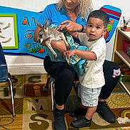 Aziel joined the competition — help win amazing prizes! toddler, woman, kangaroo, animal, child, indoor, carpet, educational_toys, chair, playroom, colorful, person, clothing, footwear, toy_shelf, interaction, curious, cute, holding, learning