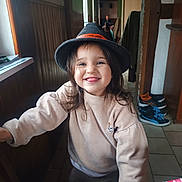 Ruby participe au concours pour gagner de l'argent avec cette photo : child, smiling, hat, indoor, wood_paneling, floor_tiles, person, tongue_out, long_hair, sweater, plaid_pants, shoes, hallway, window, tablecloth, casual_clothing, happy, portrait, cozy, blurred_background