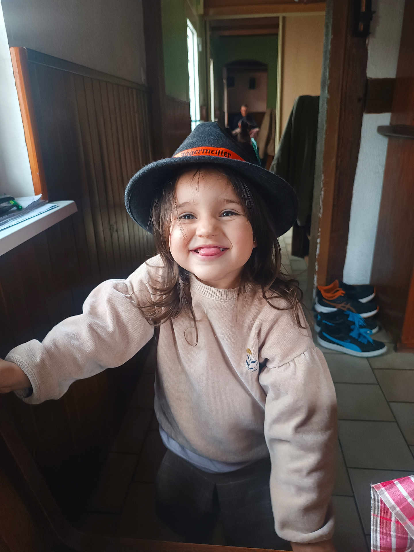 Ruby participe au concours pour gagner de l'argent avec cette photo : child, smiling, hat, indoor, wood_paneling, floor_tiles, person, tongue_out, long_hair, sweater, plaid_pants, shoes, hallway, window, tablecloth, casual_clothing, happy, portrait, cozy, blurred_background