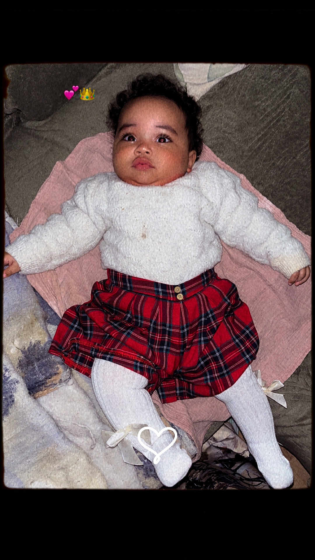 Elvira a rejoint le concours — aidez-le/la à gagner de superbes lots ! baby, child, infant, sweater, red_skirt, plaid, white_tights, blanket, couch, indoors, cute, portrait, face, eyes, expression, heart_emoji, crown_emoji, pink_blanket, soft_texture, lying_down