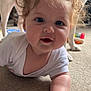 baby, child, crawling, carpet, curly_hair, dog, indoor, toy, floor, person, face, white_clothing, chubby_cheeks, pet, animal, home, play, curious, smiling, closeup