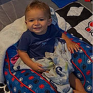 Kamdyn is registered to the contest to win money with this photo: toddler, child, smile, blanket, cushion, blue, pattern, toy, foot, hand, shirt, indoor, quilt, comfort, happy, baby, person, face, seated, home