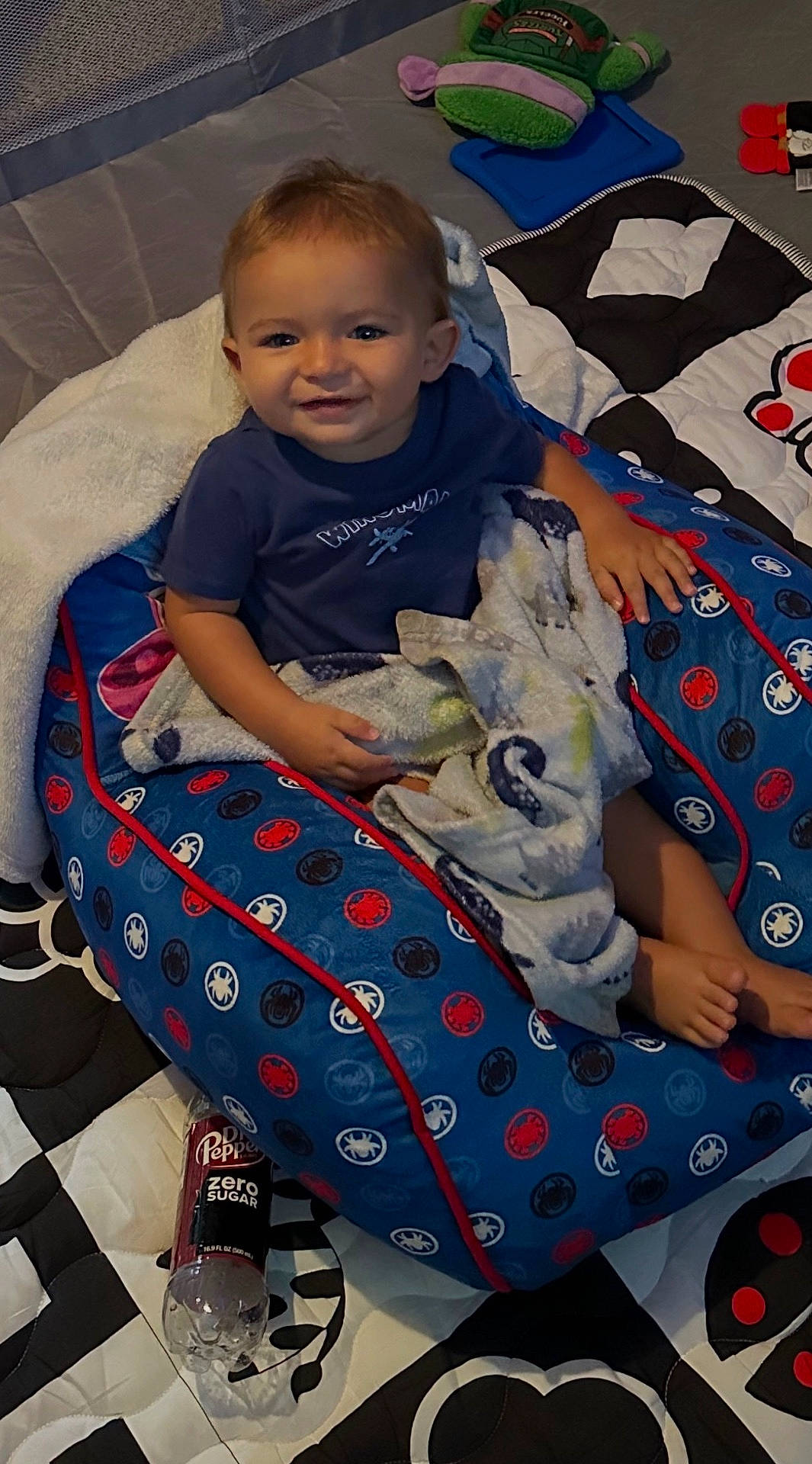 Kamdyn is registered to the contest to win money with this photo: blanket, blue_cushion, candid, casual, child, colorful, comfort, cozy, dr_pepper_bottle, floor_mat, happy, indoor, patterned, play_area, playtime, plush_toy, seated, smiling, toddler, young_child