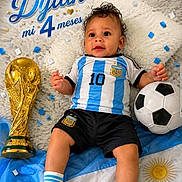 Dylan joined the competition — help win amazing prizes! baby, child, soccer_ball, trophy, confetti, blanket, blue, white, football_jersey, socks, shorts, cute, portrait, celebration, sports, argentina_flag, indoor, smiling, young_child, lying_down