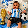 baby, child, soccer_ball, trophy, confetti, blanket, blue, white, football_jersey, socks, shorts, cute, portrait, celebration, sports, argentina_flag, indoor, smiling, young_child, lying_down