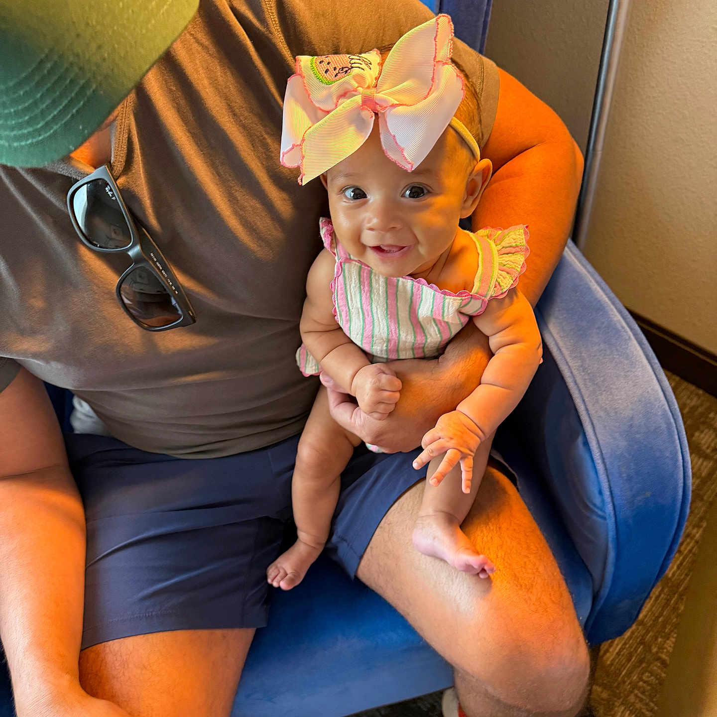 Dolly joined the competition — help win amazing prizes! adult, arm, baby, blue_chair, bow, cap, carpet, chair, child, footwear, hand, happy, indoor, orange_shoes, person, shorts, sitting, smile, striped_clothing, sunglasses