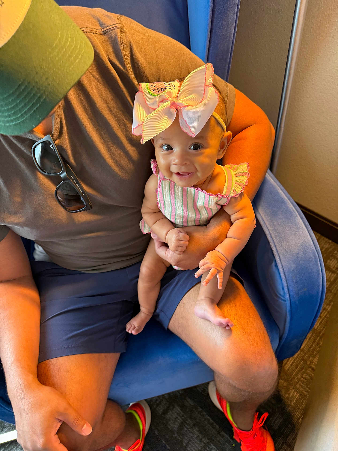 Dolly joined the competition — help win amazing prizes! baby, child, person, adult, cap, bow, smile, happy, sitting, chair, blue_chair, striped_clothing, shorts, sunglasses, footwear, orange_shoes, indoor, carpet, arm, hand