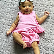 Dolly joined the competition — help win amazing prizes! baby, infant, smiling, pink_outfit, headband, floral, lying_down, quilt, textured_bedspread, cheerful, cute, small_hands, small_feet, happy, child, person, indoors, soft_lighting, portrait, one_leg_up