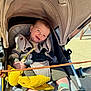 baby, child, stroller, smiling, plush_toy, harness, sunlight, blue_eyes, clothing, socks, footwear, seat, canopy, happy, infant, outdoor, cute, comfort, portrait, person