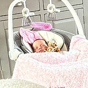 Willow is registered to the contest to win money with this photo: baby, sleeping, blanket, pink, soft_toy, rocker, infant, indoor, cabinet, frame, decor, cozy, child, nursery, resting, comfort, home, furniture, toddler, peaceful