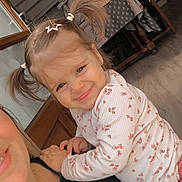 Mia participe au concours pour gagner de l'argent avec cette photo : adult, casual, chair, child, clothing, expression, face, furniture, hair_clip, happy, holding, indoor, long_sleeve, patterned_shirt, person, pigtails, smile, table, toddler, wooden_floor