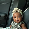 baby, child, infant, car_seat, car_interior, seated, portrait, smiling, happy, headwrap, topknot, leopard_print, dress, blanket, seatbelt, vehicle, indoor, closeup, adorable, face