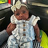 Kyla is registered to the contest to win money with this photo: baby, infant, child, portrait, car_seat, car_interior, bow_headband, dress, overalls, striped_clothing, buttons, sitting, brown_skin, dark_hair, large_eyes, serious_expression, window, sunlight, toy, travel