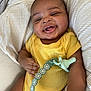 baby, infant, smiling, yellow_onesie, pacifier, pacifier_clip, striped_pillow, blanket, hand, face, happy, cute, child, indoors, person, closeup, relaxing, lying_down, skin, young_child