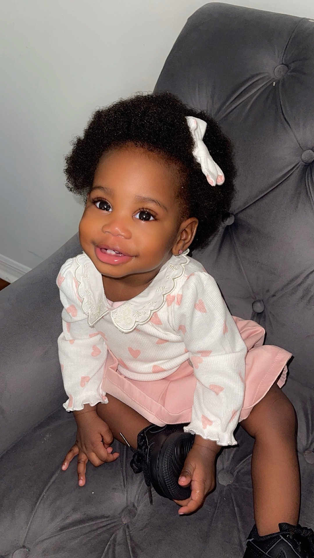 Faith is registered to the contest to win money with this photo: toddler, child, smiling, curly_hair, bow, white_top, pink_skirt, black_shoes, chair, indoor, cute, happy, portrait, fashion, person, seated, baby, hand, face, eyelashes
