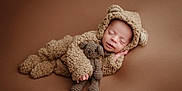 Samuel is registered to the contest to win money with this photo: baby, sleeping, costume, bear, plush, knitted_toy, teddy_bear, infant, cute, cozy, brown_background, soft_texture, portrait, child, adorable, newborn, hand, face, closed_eyes, lying_down