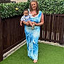 baby, backyard, barefoot, bee_ornaments, blue_dress, casual, child, dress, family, fence, grass, happy, holding, leaf_decorations, outdoor, person, photography, portrait, smile, woman