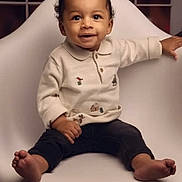 Kobie is registered to the contest to win money with this photo: toddler, child, smiling, barefoot, white_chair, sweater, indoor, portrait, cute, happy, baby, person, window, wooden_legs, floor, modern_chair, cozy, warm_lighting, seated, casual_clothing