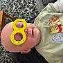 baby, child, bald, toy, yellow, goggles, face, onesie, winnie_the_pooh, cartoon, carpet, phone, couch, indoor, person, cute, playful, infant, clothing, smile