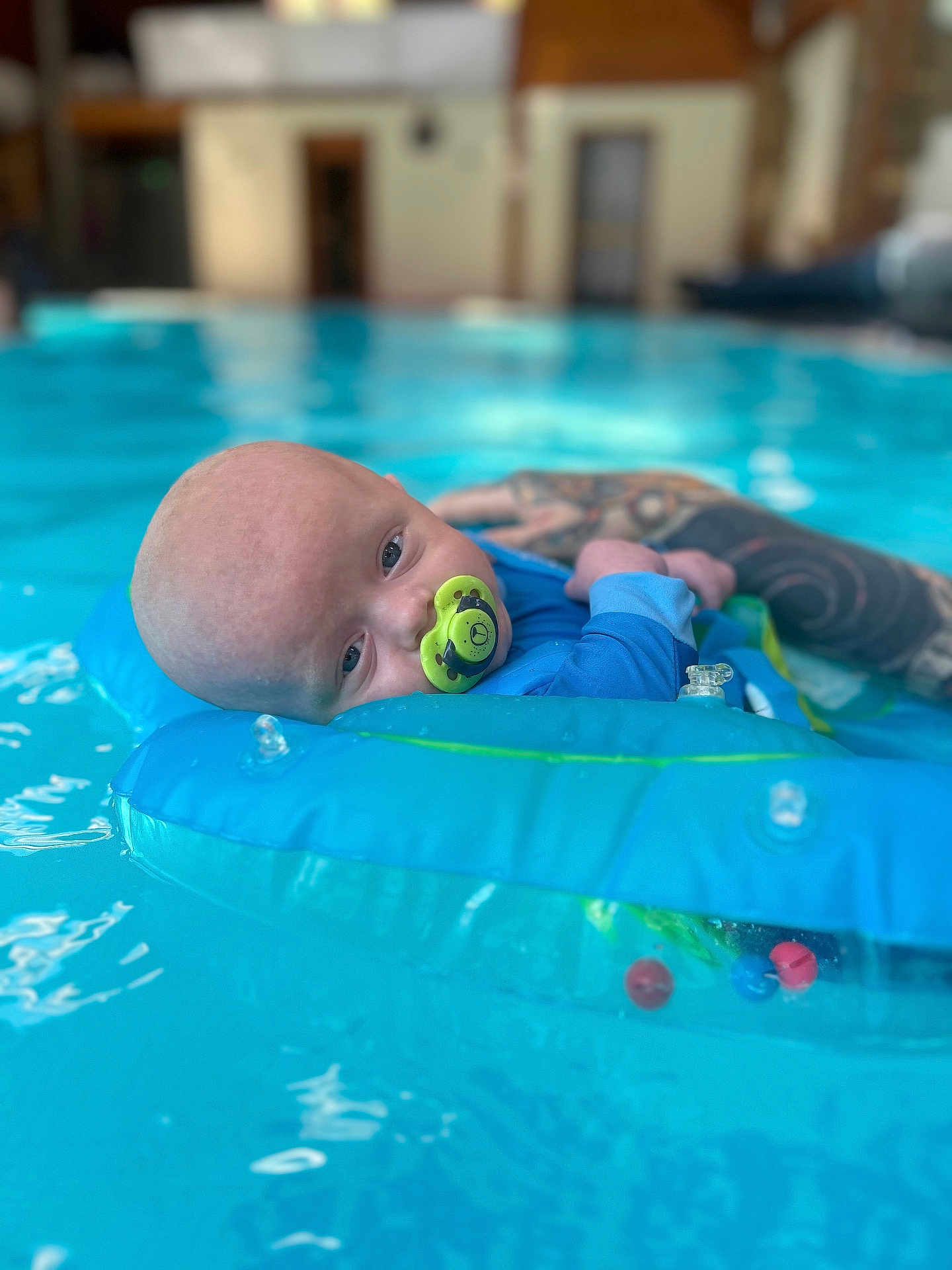 Koda-Bear joined the competition — help win amazing prizes! baby, infant, pool, water, float, inflatable_ring, pacifier, tattoo, arm, blue_clothing, swimming, indoor_pool, relaxation, child, support, calm, portrait, closeup, person, water_sport