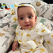 Praavi is registered to the contest to win money with this photo: baby, infant, child, headband, yellow_hearts, onesie, cushion, animal_print, giraffe, elephant, zebra, bed, bedding, curious_expression, indoors, portrait, cute, soft, cozy, smiling