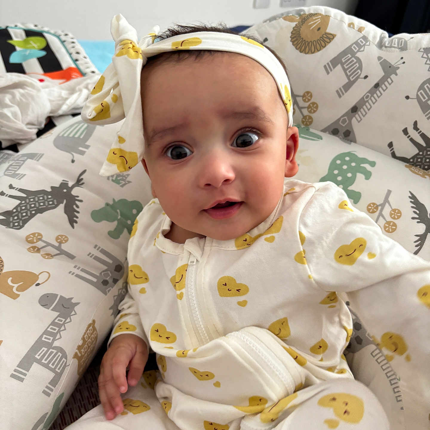 Praavi is registered to the contest to win money with this photo: animal_print, baby, bed, bedding, child, cozy, curious_expression, cushion, cute, elephant, giraffe, headband, indoors, infant, onesie, portrait, smiling, soft, yellow_hearts, zebra