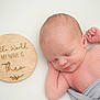Theo is registered to the contest to win money with this photo: newborn, baby, sleeping, infant, wooden_sign, text, gray_cloth, soft_light, peaceful, portrait, child, cute, resting, skin, close_up, head, hand, white_background, name_sign, baby_boy