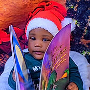Noah is registered to the contest to win money with this photo: toddler, child, santa_hat, book, reading, holiday, christmas, festive, cozy, indoor, pajamas, smiling, face, person, decorations, tree, winter, cute, happy, warm