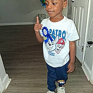 Jayceon is registered to the contest to win money with this photo: child, boy, toddler, portrait, standing, thumbs_up, smiling, indoors, hallway, door, balloons, birthday, t_shirt, cartoon, sneakers, blue_pants, wood_floor, home, celebration, face
