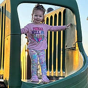 Kinley is registered to the contest to win money with this photo: child, girl, playground, slide, pink_shirt, curly_hair, smiling, outdoor, sunlight, play, fun, happy, casual_clothing, legs, footwear, daytime, park, structure, person, cute