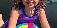 Kinley is registered to the contest to win money with this photo: child, girl, curly_hair, pony_tails, purple_clothing, beach_volleyball, outdoor, sunlight, happy, smiling, playful, sports_equipment, summer, recreation, fun, young_child, active, colorful, portrait, close_up