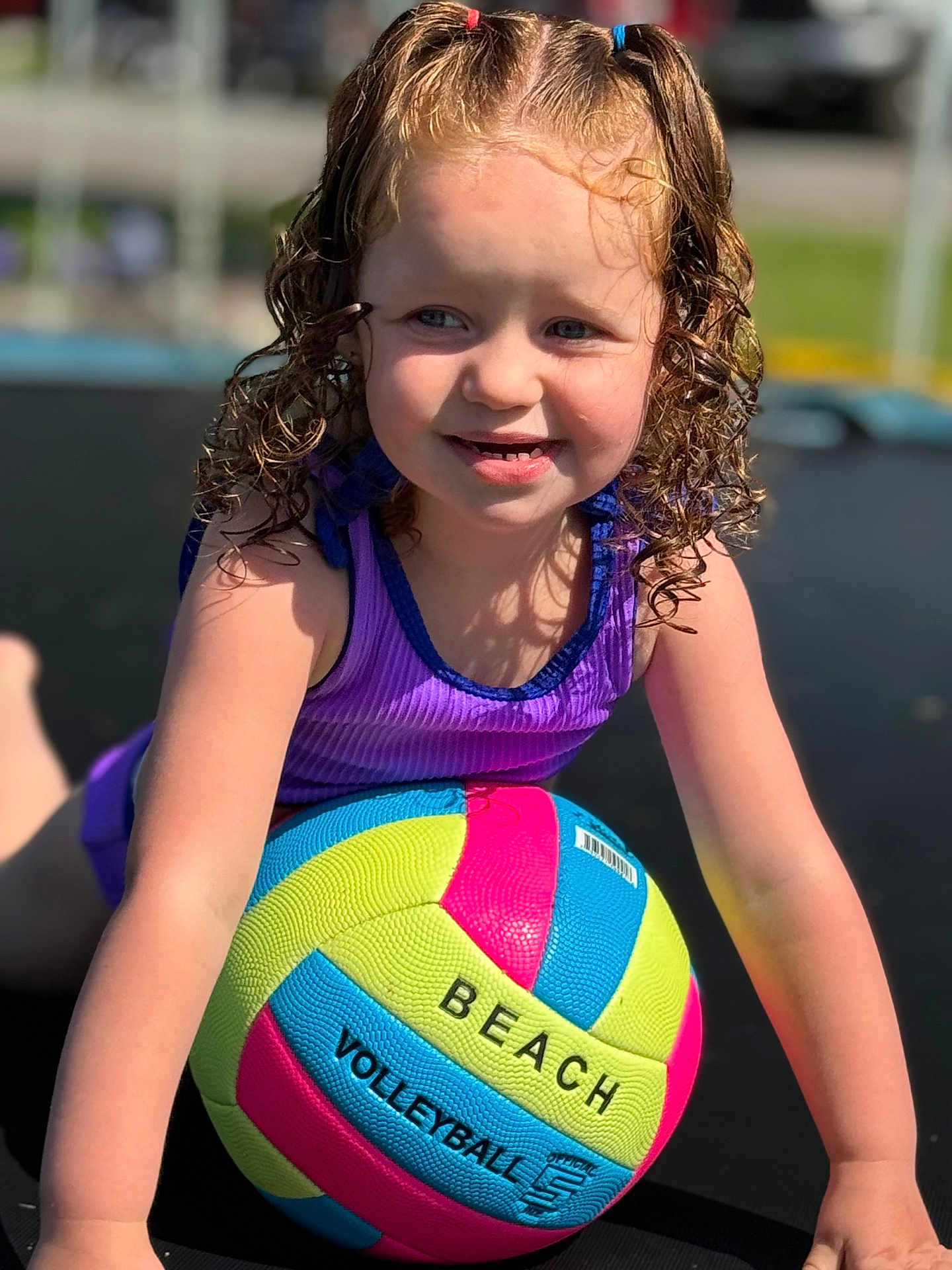 Kinley is registered to the contest to win money with this photo: child, girl, curly_hair, pony_tails, purple_clothing, beach_volleyball, outdoor, sunlight, happy, smiling, playful, sports_equipment, summer, recreation, fun, young_child, active, colorful, portrait, close_up