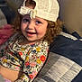 Kinley is registered to the contest to win money with this photo: child, toddler, smiling, curly_hair, hat, cap, floral_clothing, long_sleeve, pillow, indoor, cozy, happy, person, portrait, cute, young_child, sitting, face, casual, relaxed