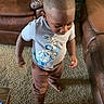 toddler, child, standing, indoors, living_room, leather_chair, carpet, toy, astronaut_shirt, brown_pants, short_hair, looking_down, walking, portrait, home, furniture, floor, casual_clothing, cute, daylight