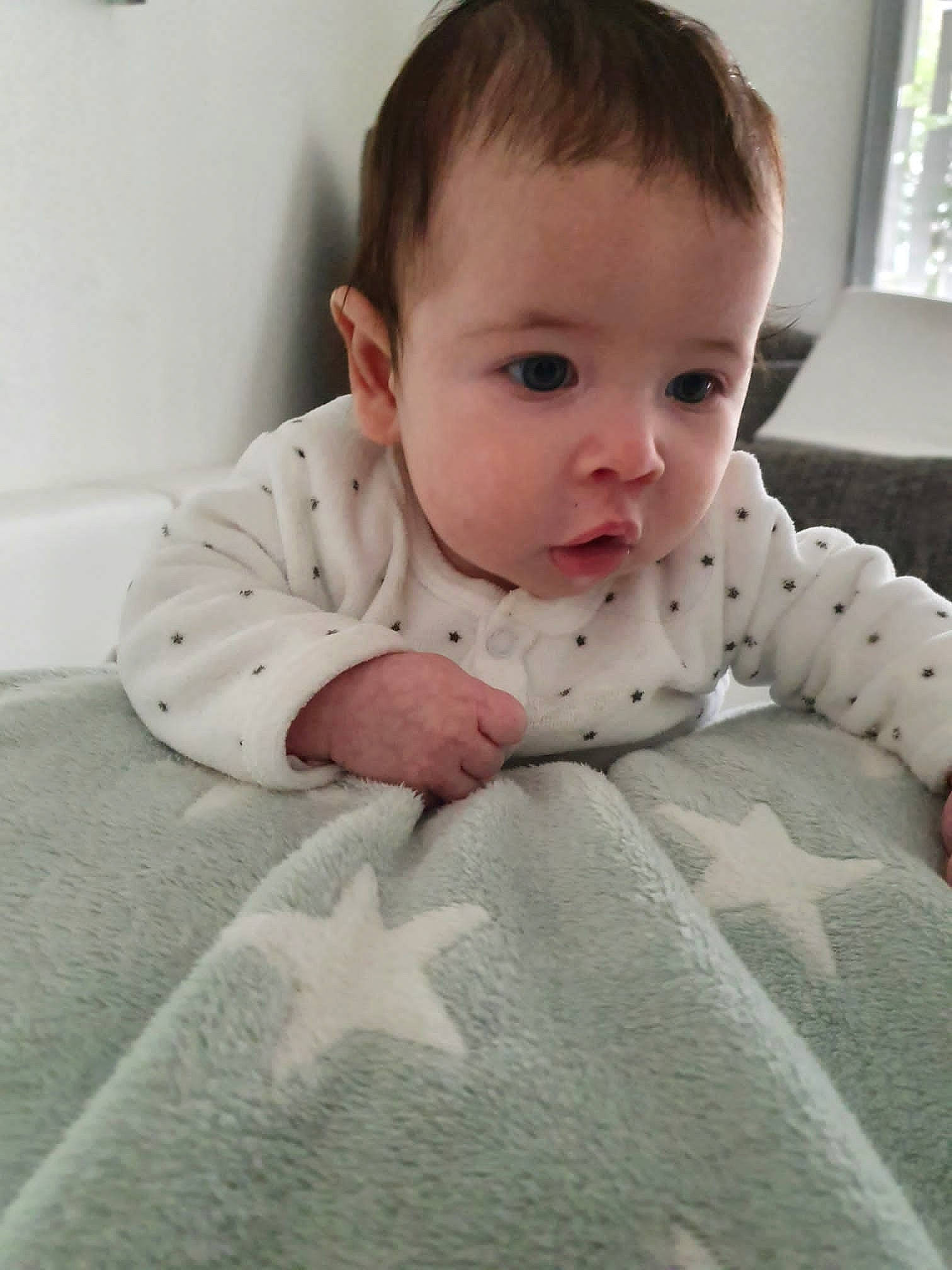 Malöe participe au concours pour gagner de l'argent avec cette photo : arm, baby, baby_toddler_clothing, bedding, cheek, child, comfort, crawling, floor, flooring, grey, head, iris, linens, pattern, person, sitting, sleeve, surprise, toddler