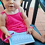 barefoot, book, chair, child, curious, daylight, expression, face, outdoor, pen, person, pink_dress, plastic_chair, portrait, reading, sitting, tile_floor, toddler, writing, young_child
