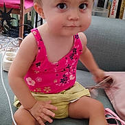 Mia a rejoint le concours — aidez-le/la à gagner de superbes lots ! toddler, child, indoor, sitting, pink_top, yellow_shorts, curly_hair, glasses, couch, carpet, furniture, book, chair, cute, portrait, young_child, casual, expression, person, home