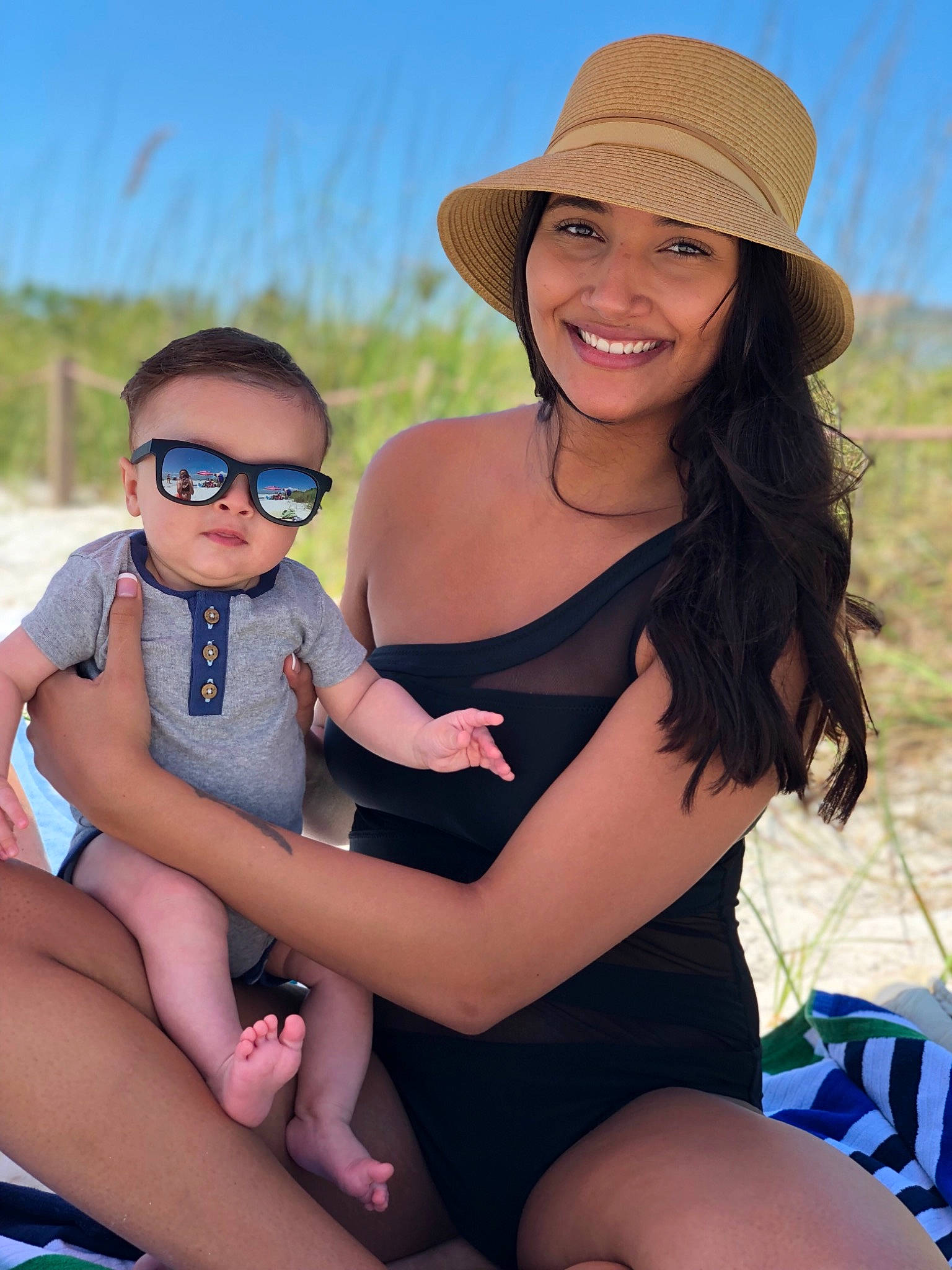 Grant is registered to the contest to win money with this photo: beach, beauty, child, clothing, eyewear, fashion, glasses, grass, hat, headgear, headwear, joy, leg, long_hair, people, person, photography, sitting, smile, summer