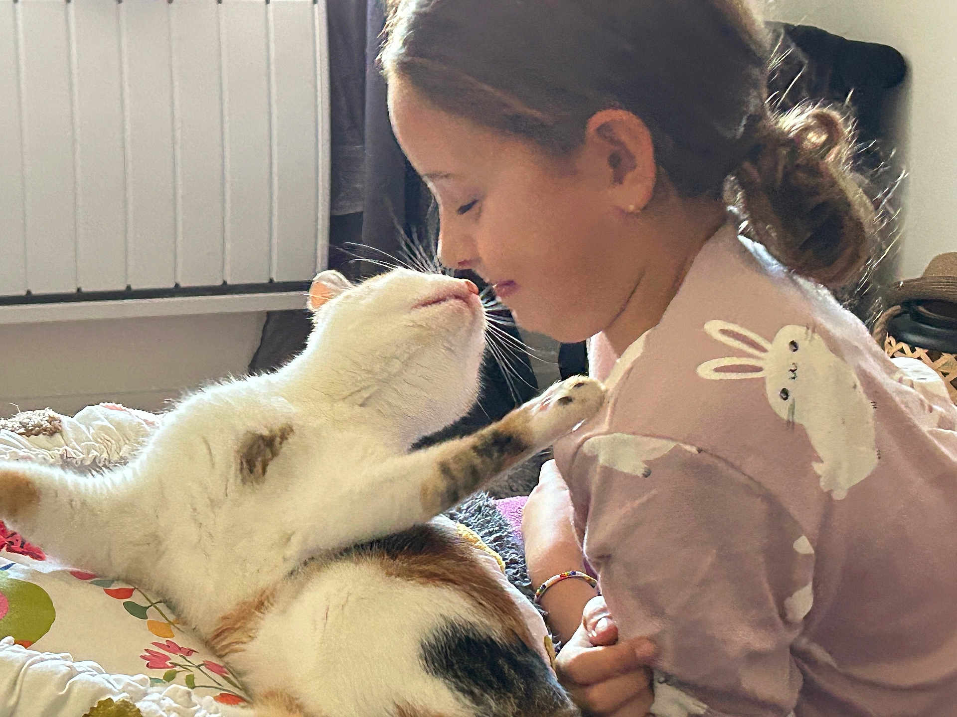 Lila a rejoint le concours — aidez-le/la à gagner de superbes lots ! cat, child, indoor, interaction, cute, smile, animal, pet, girl, shirt, bunny_print, bed, cozy, affection, paw, face, closeup, relaxed, feline, human