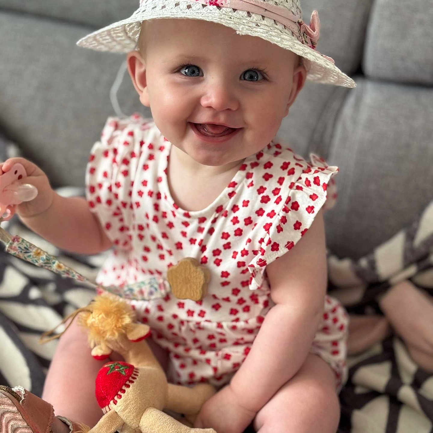 Lilou participe au concours pour gagner de l'argent avec cette photo : baby, blanket, blue_eyes, child, closeup, cute, happy, hat, indoor, infant, pacifier, patterned_clothing, person, pink, plush_toy, red, sitting, smiling, soft_toy, white
