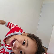 Jahime participe au concours pour gagner de l'argent avec cette photo : child, smiling, indoor, curly_hair, red_sweater, striped_clothing, happy, portrait, playful, bedroom, face, person, young, casual_clothing, expression, head, joyful, closeup, skin, eyes