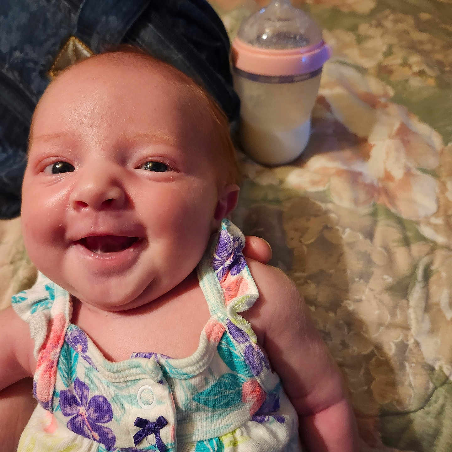 Willow is registered to the contest to win money with this photo: arm, baby, bedspread, bottle, child, closeup, colorful, cute, dress, fabric, floral, hand, happy, indoors, infant, pattern, person, portrait, skin, smiling