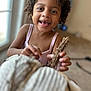 background_blur, child, clothing, curly_hair, cute, expression, focus, happy, holding, indoor, natural_light, person, playful, portrait, skin, smiling, toddler, twigs, window, young
