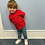 child, toddler, red_shirt, blue_jeans, white_sneakers, smiling, standing, indoor, playful, casual_clothing, hair, wall, floor, tile_floor, portrait, cute, young_child, happy, person, footwear