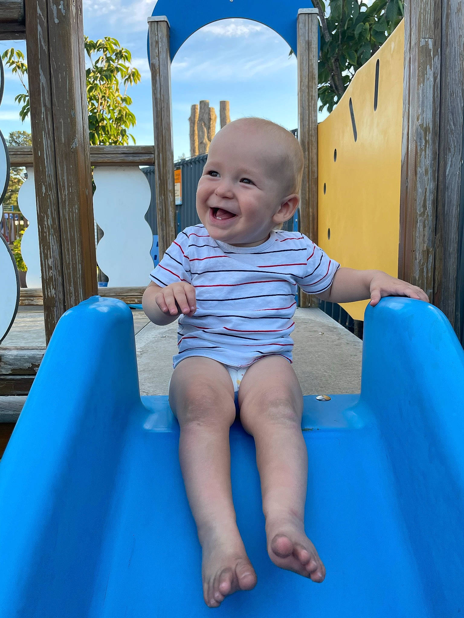 Emilio a rejoint le concours — aidez-le/la à gagner de superbes lots ! aqua, azure, baby_toddler_clothing, blue, chute, city, facial_expression, fun, happy, human_body, joy, leisure, person, pink, playground, recreation, skin, sky, smile, standing