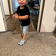Malachi is registered to the contest to win money with this photo: black_shirt, carpet, chair, child, curly_hair, cute, denim_shorts, doorway, floor, furniture, happy, home, indoor, living_room, person, shoes, smiling, toddler, walking, wood_floor